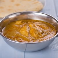 Creamiges Chicken Korma in silberner Schale mit Fladenbrot im Hintergrund – India4U Bern